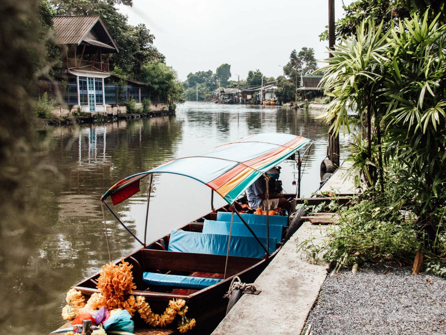 Ein Longtailboot mit bunter Plane liegt am Ufer des Flusses durch Bangkok.