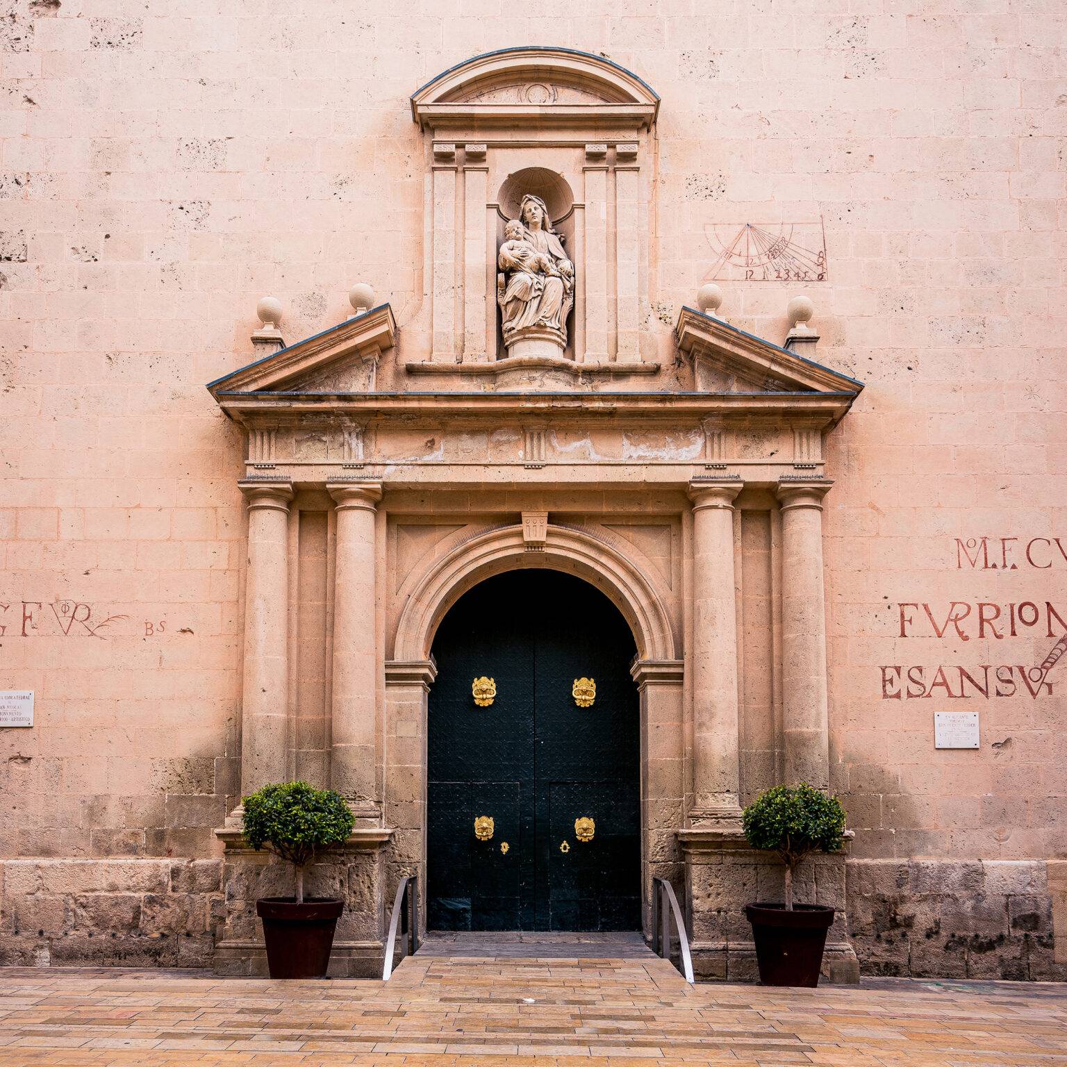 Eingang einer Kirche mit schwarzer Tür und einer Marienfigur in der Altstadt von Alicante.