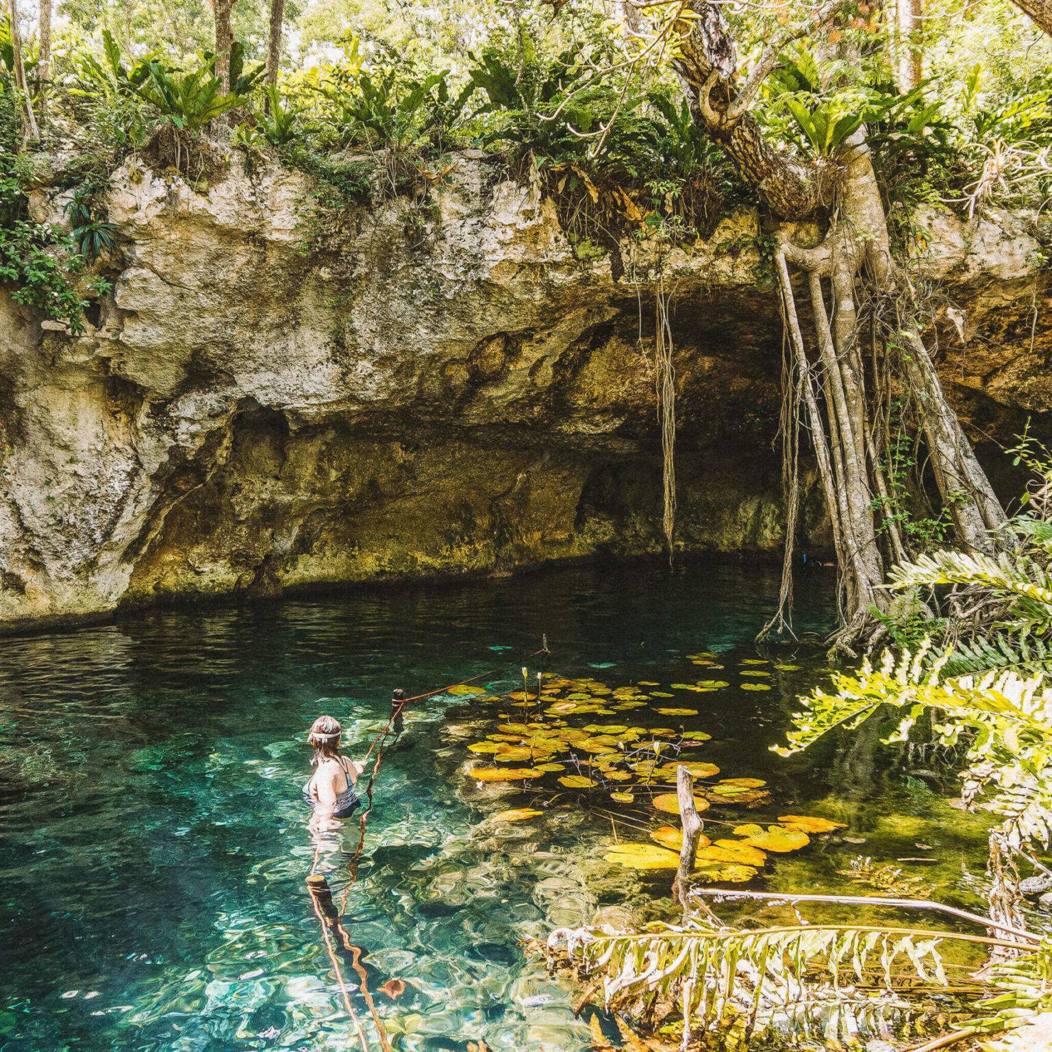 Eine Frau schwimmt in der Gran Cenote in Tulum auf Yucatan und blickt in Richtung einer Höhle.