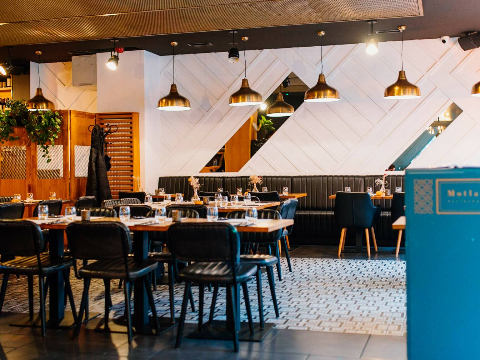 Das modern eingerichtete Restaurant Motlava in Danzig schmücken schwarze Stühlen, Holztischen und goldene Hängelampen.
