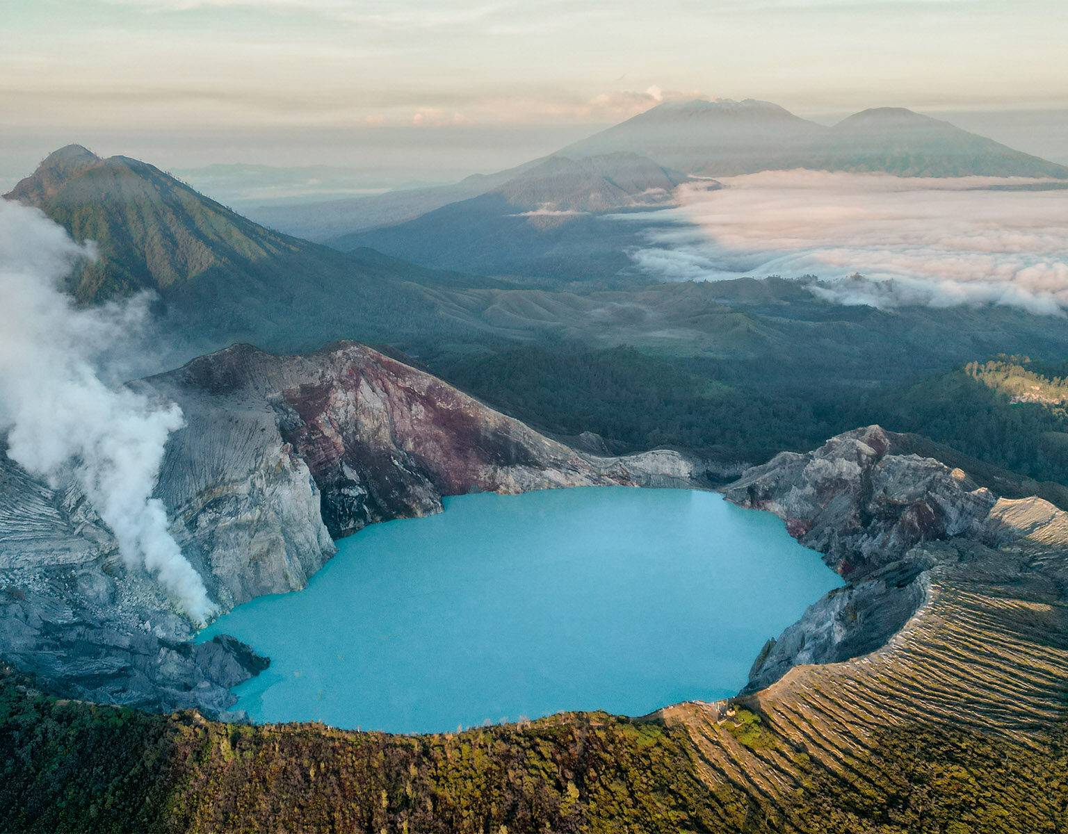 Ein türkisblauer See im Vulkan Ijen in Java, im Hintergrund begrünte Berge.