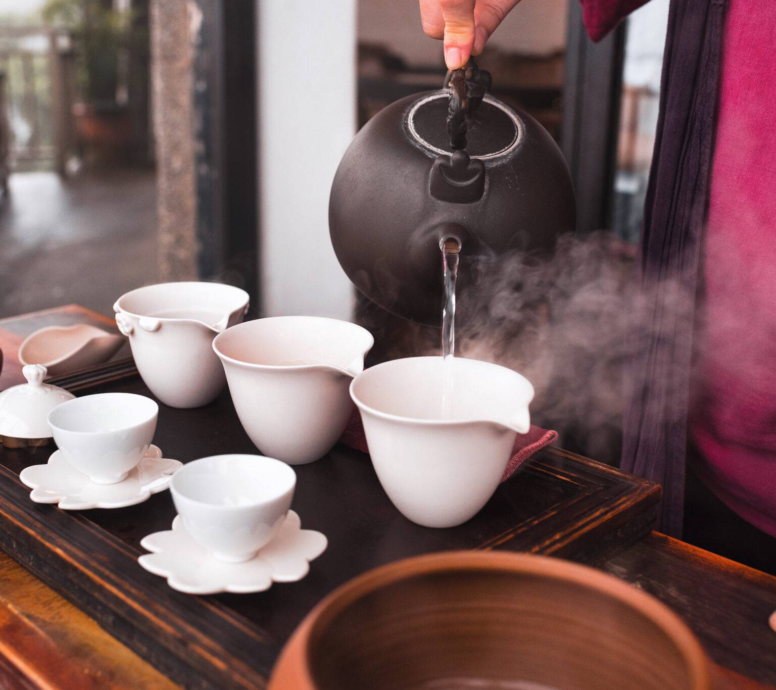 Kochendes Wasser wird aus einer schwarzen Teekanne in weißen Tassen geschüttet.
