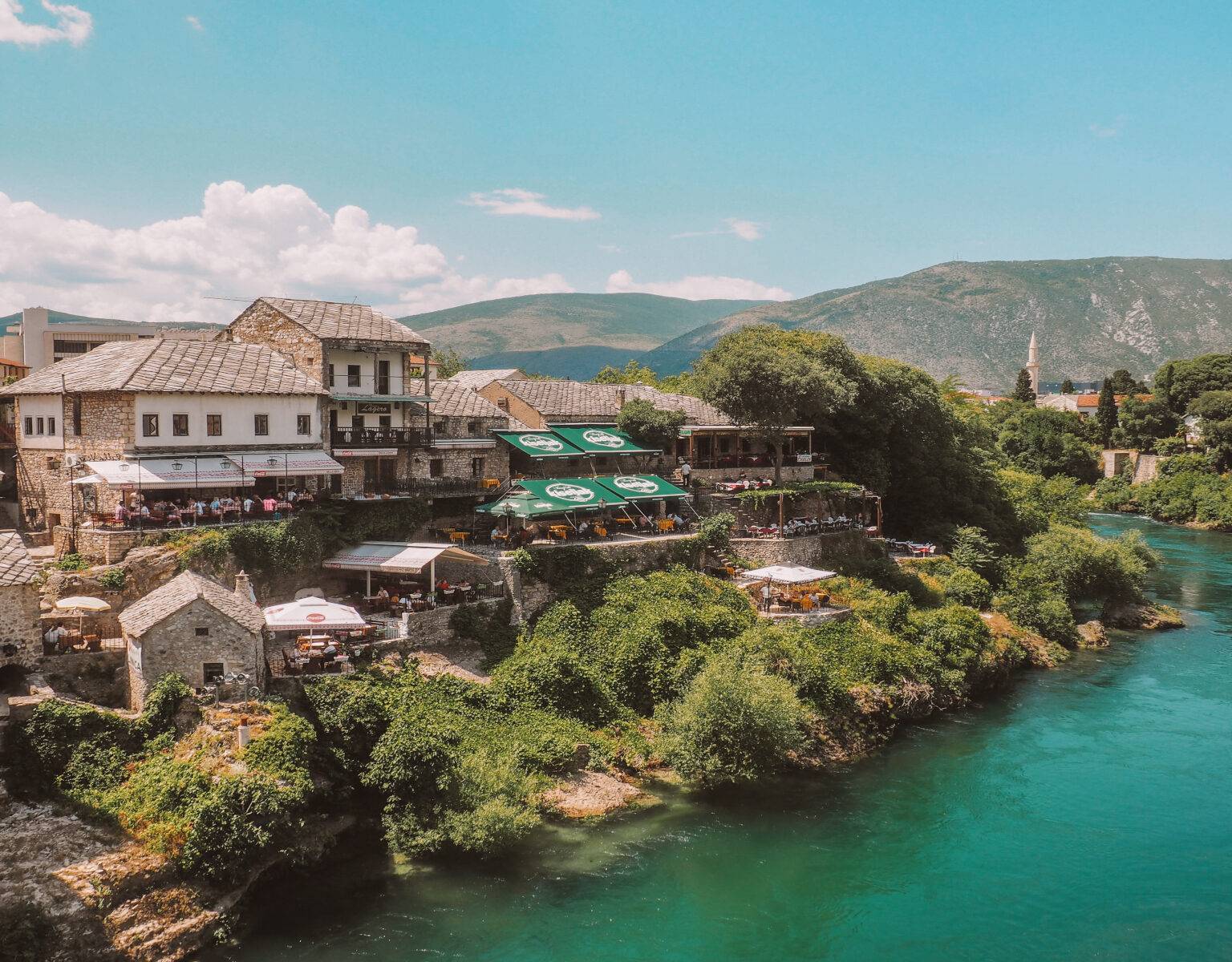 Ein satt-türkiser Fluss schlängelt sich entlang eines Dorfes in Bosnien und Herzegowina.