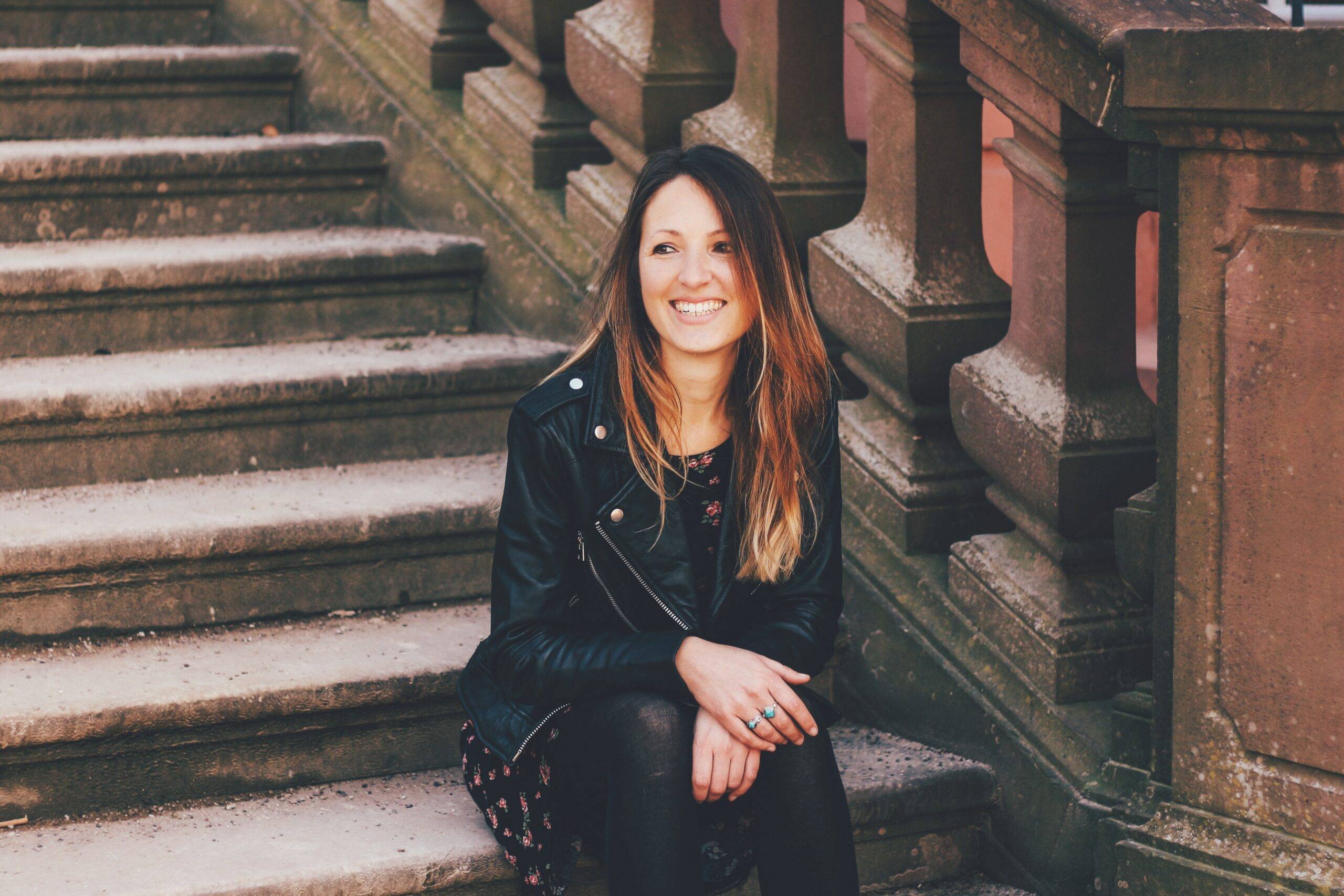 Reisebloggerin Sarah vom Blog Itchy Feet sitzt lächelnd auf einer Steintreppe.