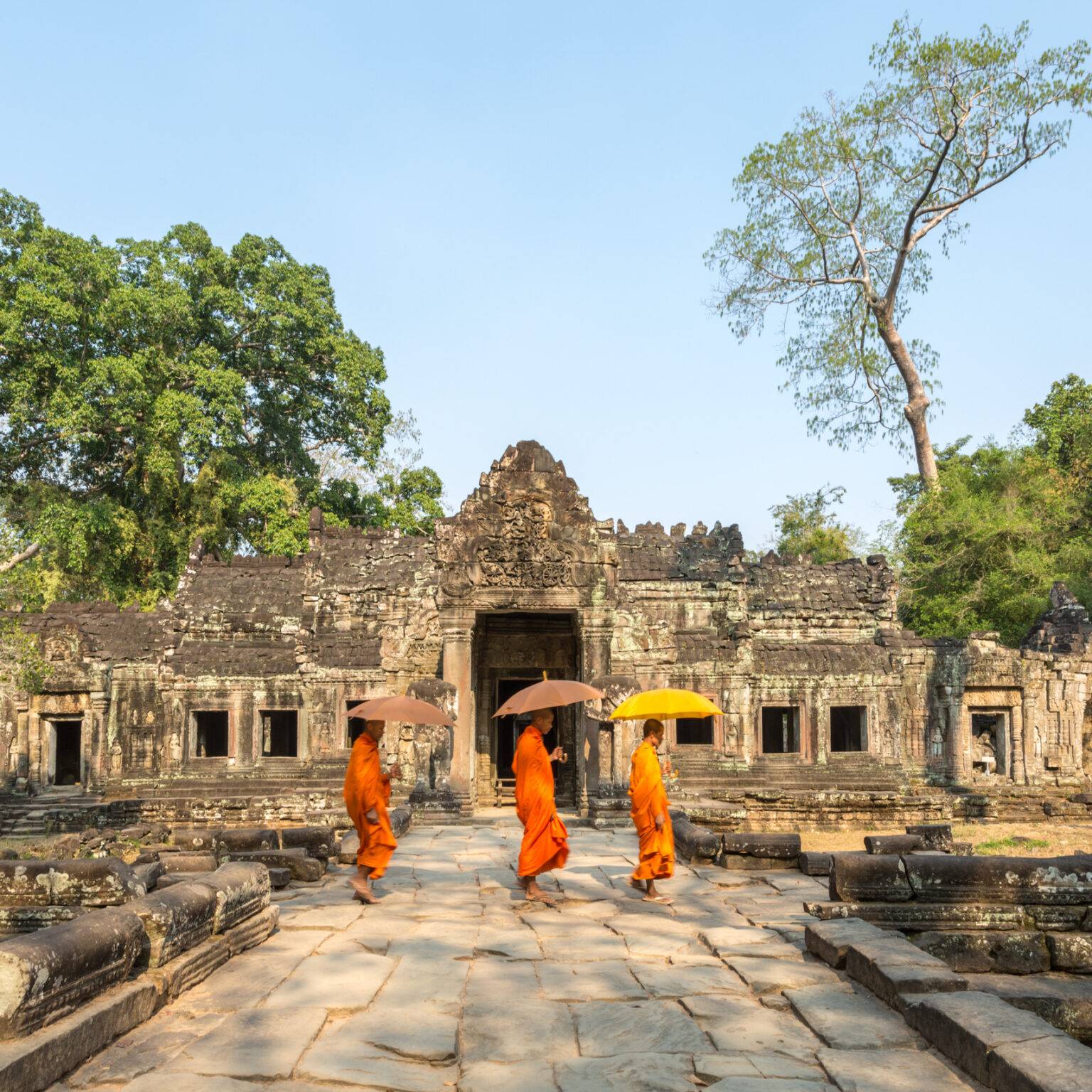 Drei Mönche laufen vor dem Angkor Wat Tempel.