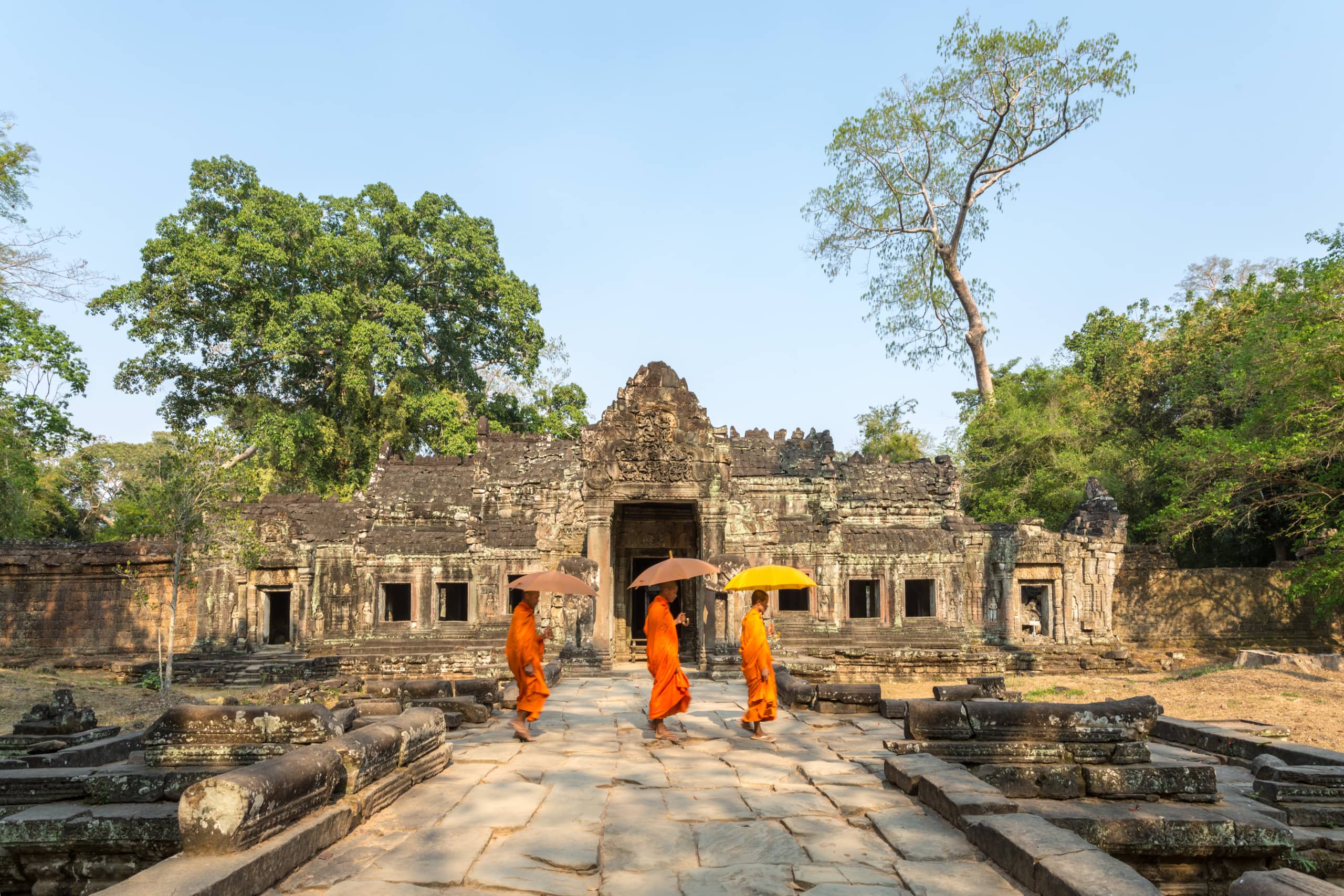 Drei Mönche laufen vor dem Angkor Wat Tempel.