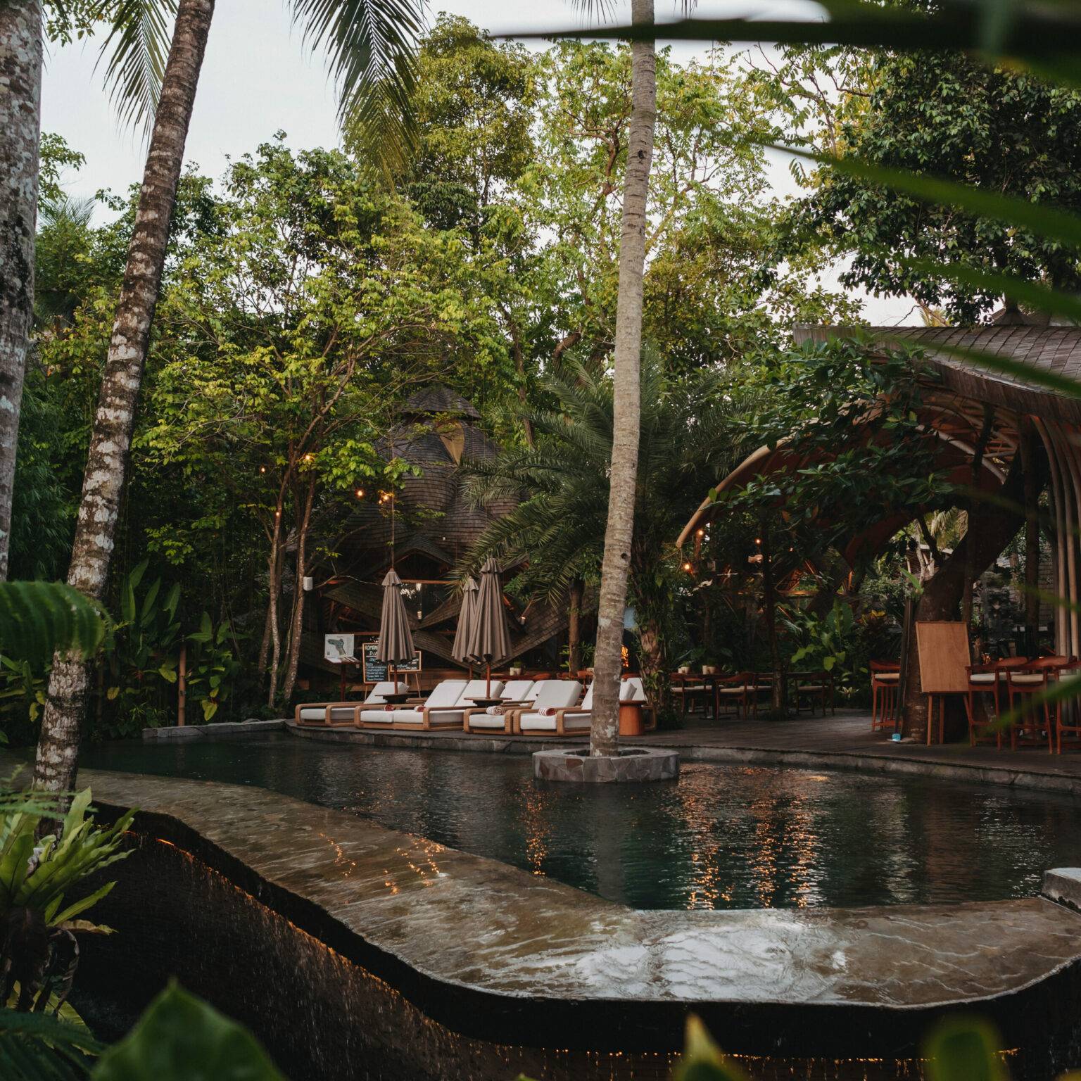 Liegeflächen im Ulaman Bali laden am Pool umgeben von Grün zum Entspannen ein.