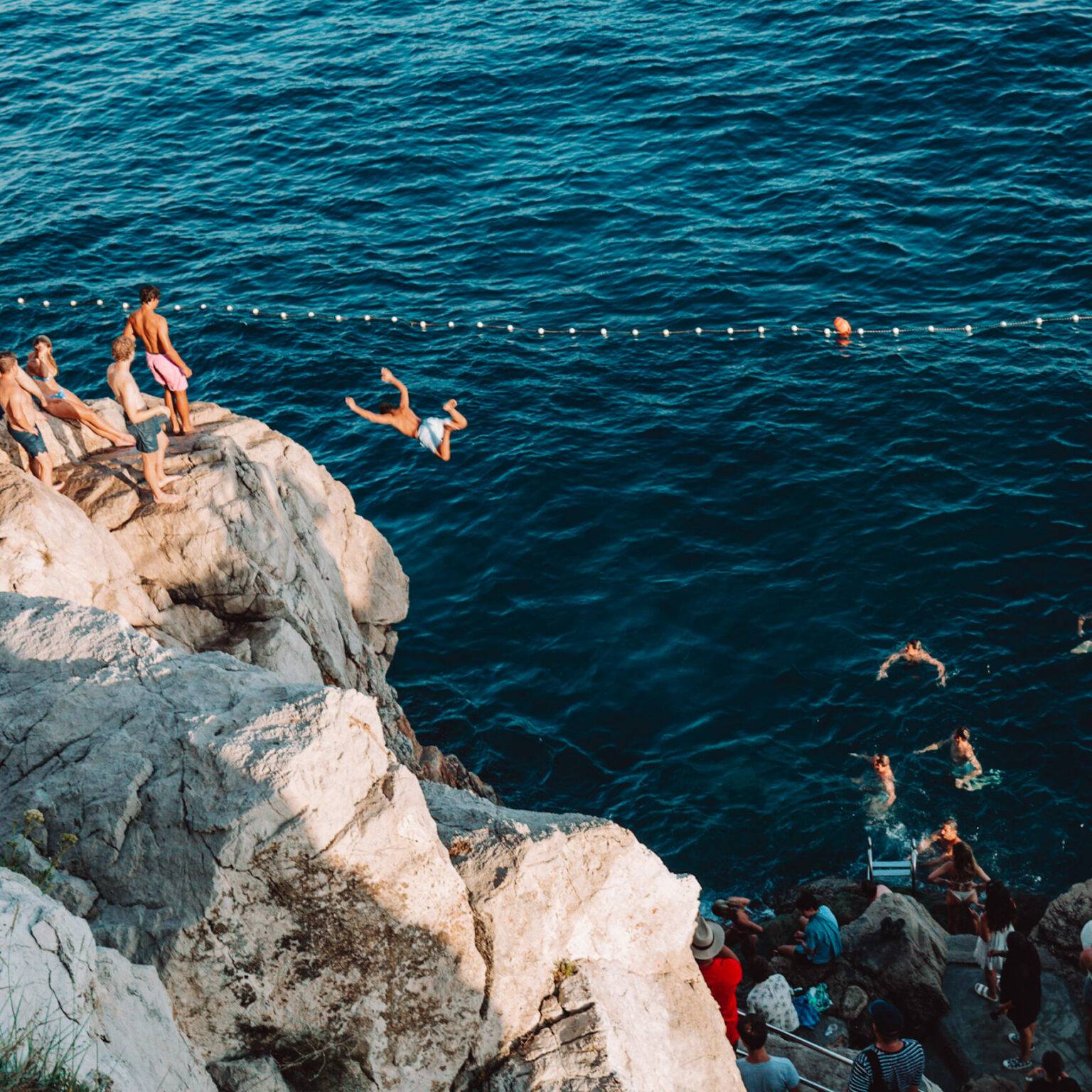 Menschen springen von einer Klippe in das Meer.