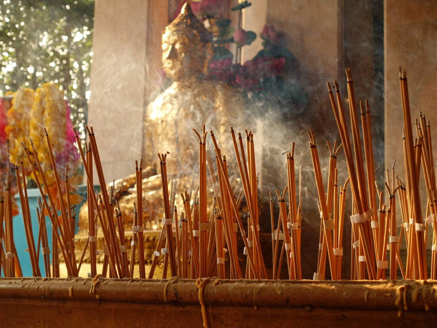 Der Rauch der angezündeten Räucherstäbchen in einem buddhistischen verschleiern den Blick auf eine Buddha-Statue.