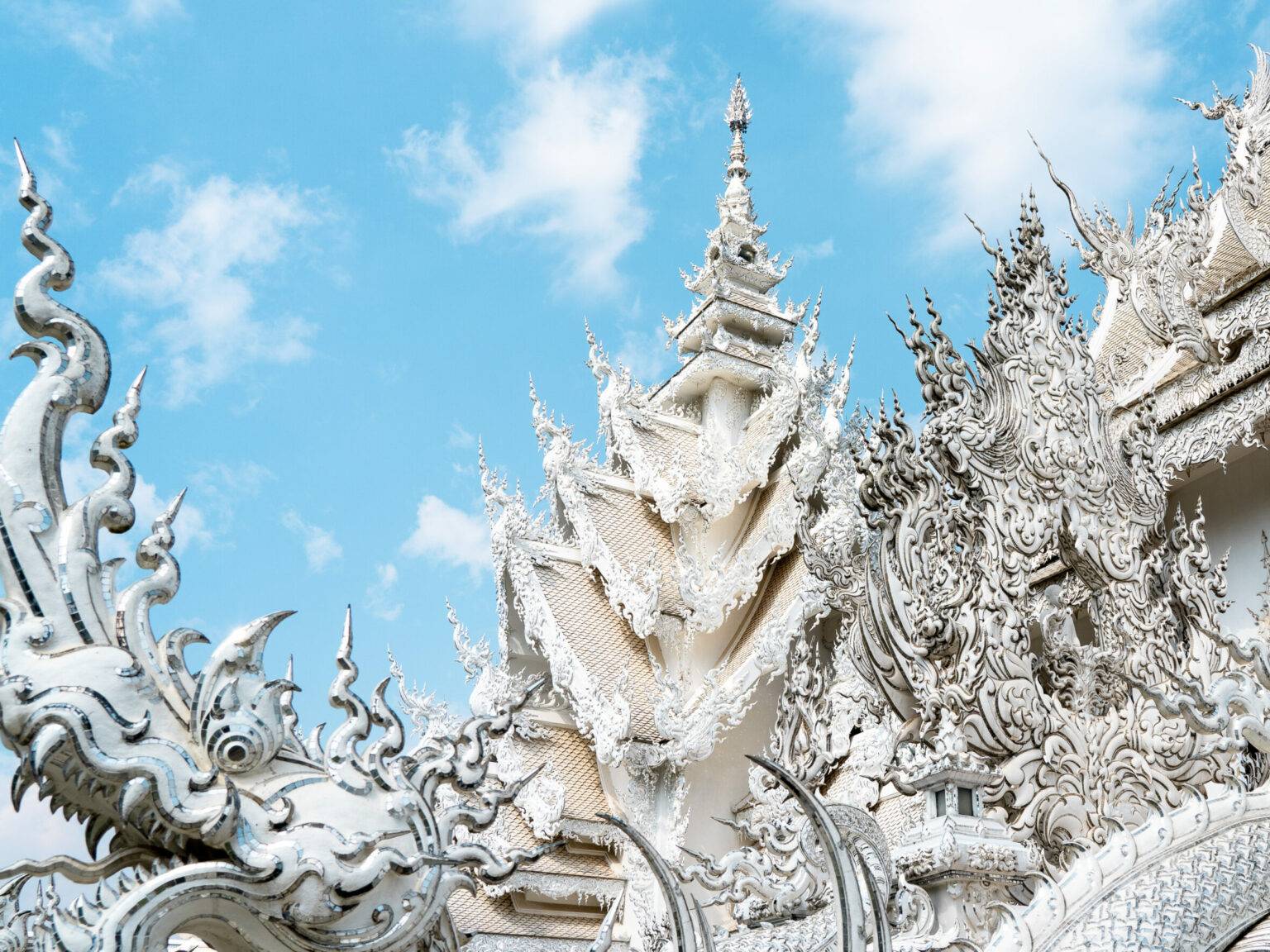 Drachenköpfe, spitze Türme und ausgefallene Spiegelstücke verzieren den weißten Tempel in Chiang Rai.