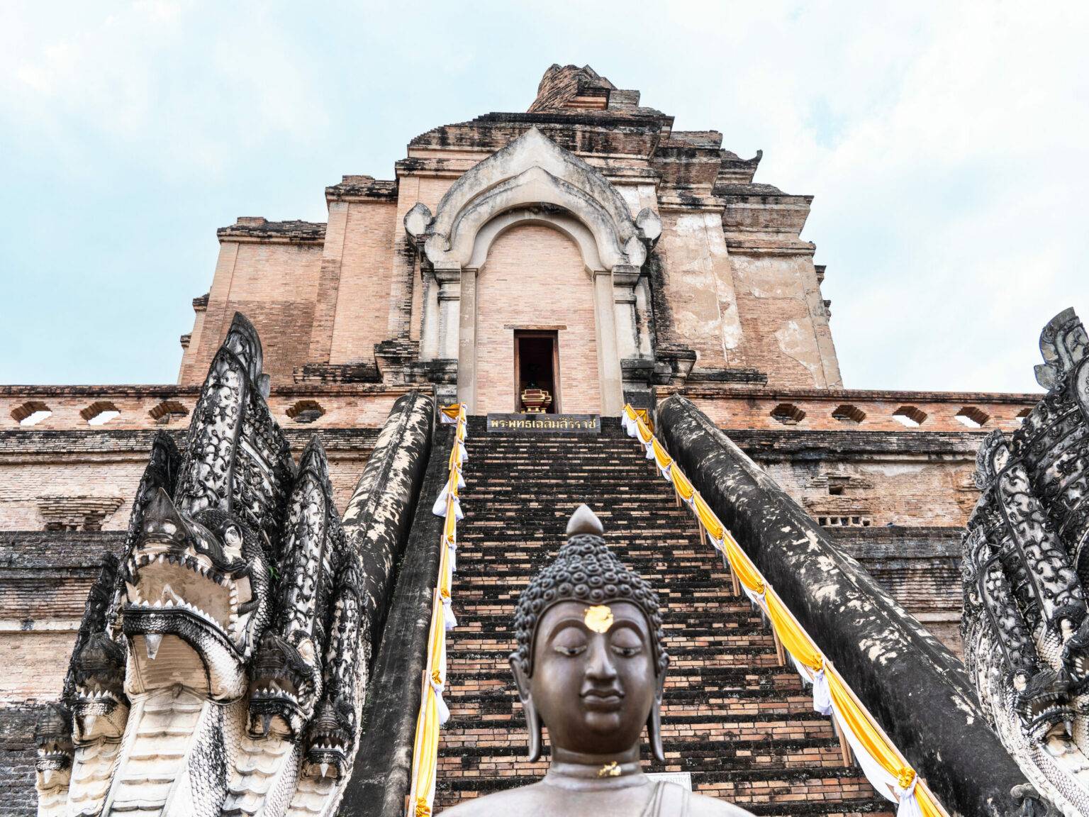 Eine Buddha-Statue steht vor den Stufen eines Tempels.