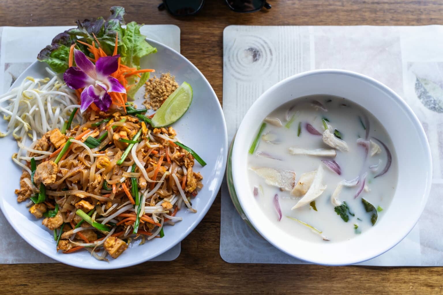 Links auf dem Teller ist das traditionelle Nudelgericht Pad Thai zubereitet, in der Schüssel rechts die Currysuppe Tom Kha Gai.