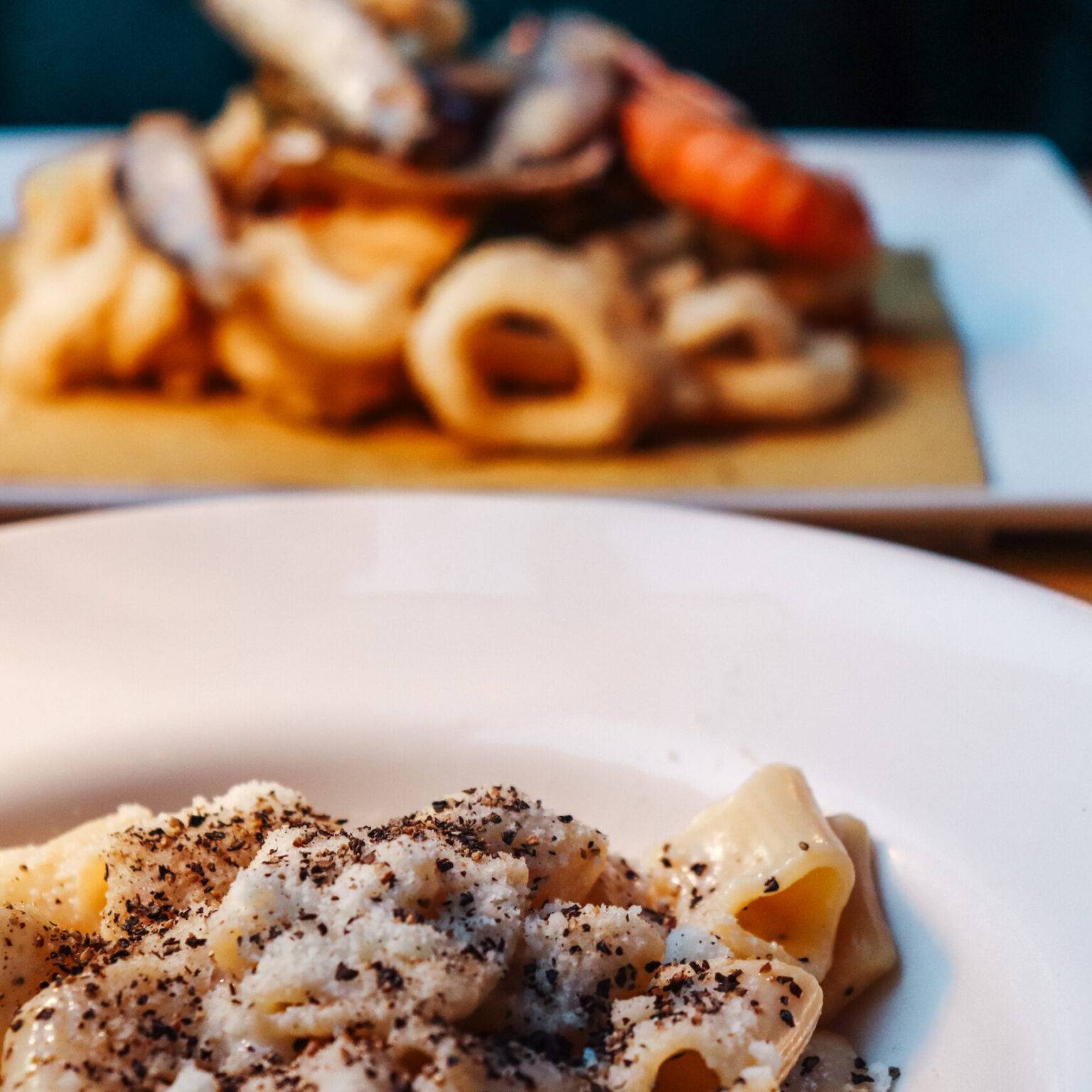 Im Vordergrund Cacio e Pepe, im Hintergrund frittierte Meeresfrüchte.