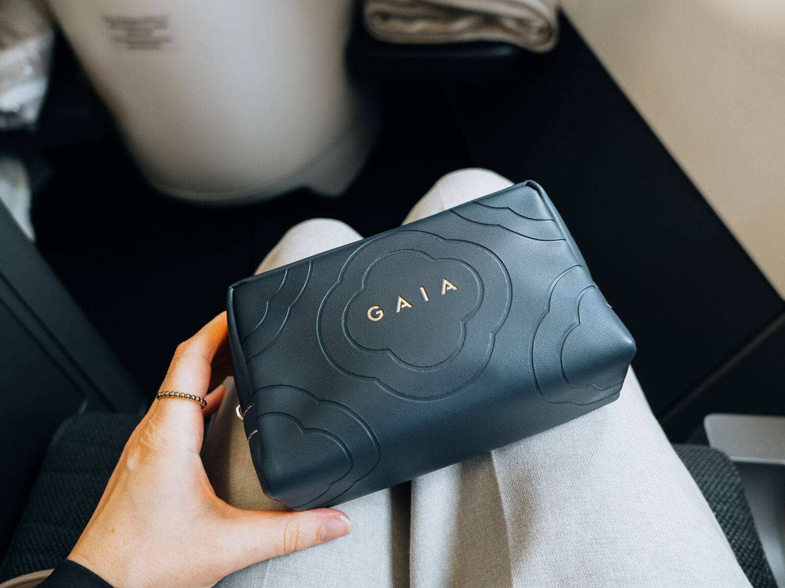 Schwarze Lederhandtasche der Marke Gaia mit graviertem Logo auf einem Sitzplatz im Flugzeug.