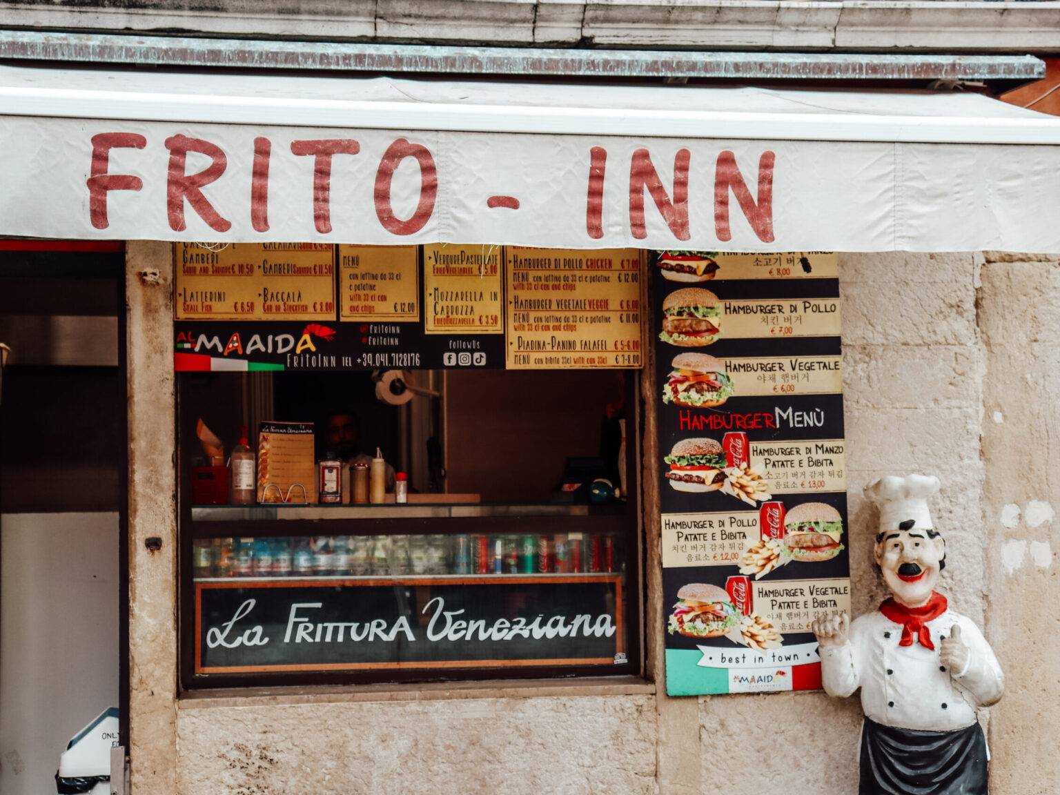Der Imbiss Frito Inn von außen mit weißer Markise und einer kleine Pizza-Bäcker-Figur.