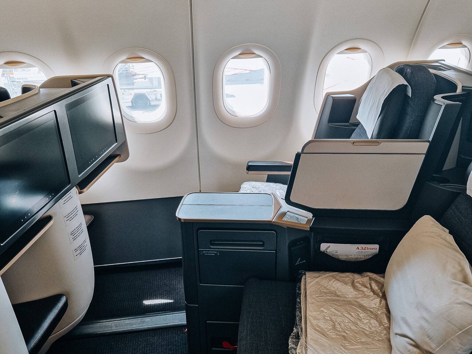 Zwei nebeneinanderliegende Business-Class-Sitze in einem Flugzeug mit Mittelarmlehne, Tisch und großen Fenstern.