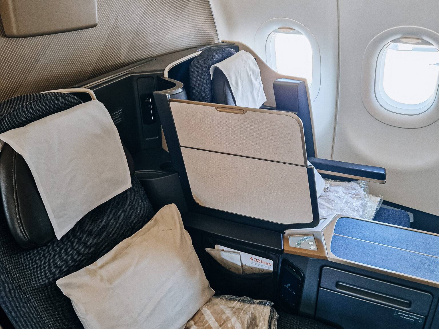 Zwei nebeneinanderliegende Flugzeugsitze in Business Class mit Kopfstützen, Armlehnen und einem Notausgang-Fenster im Hintergrund.