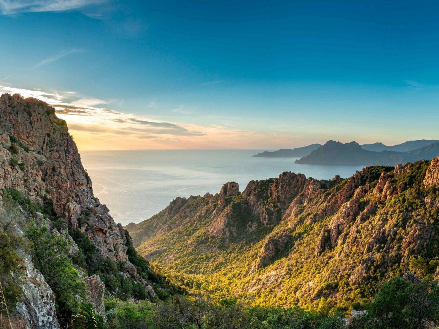 Die untergehende Sonne über dem Mittelmeer wirft ihr Licht auf die grün bewachsenen Hänge an der Ostküste Korsikas.