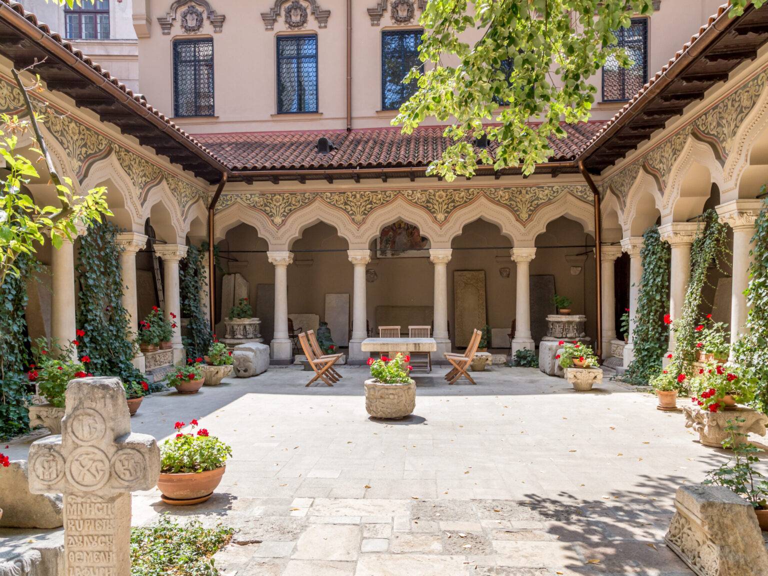 Der Innenhof des Klosters Stavropoleos in Bukarest mit vielen mit Efeu bewachsenen Säulen, spitz zulaufenden Torbögen und detaillierten Verzierungen.