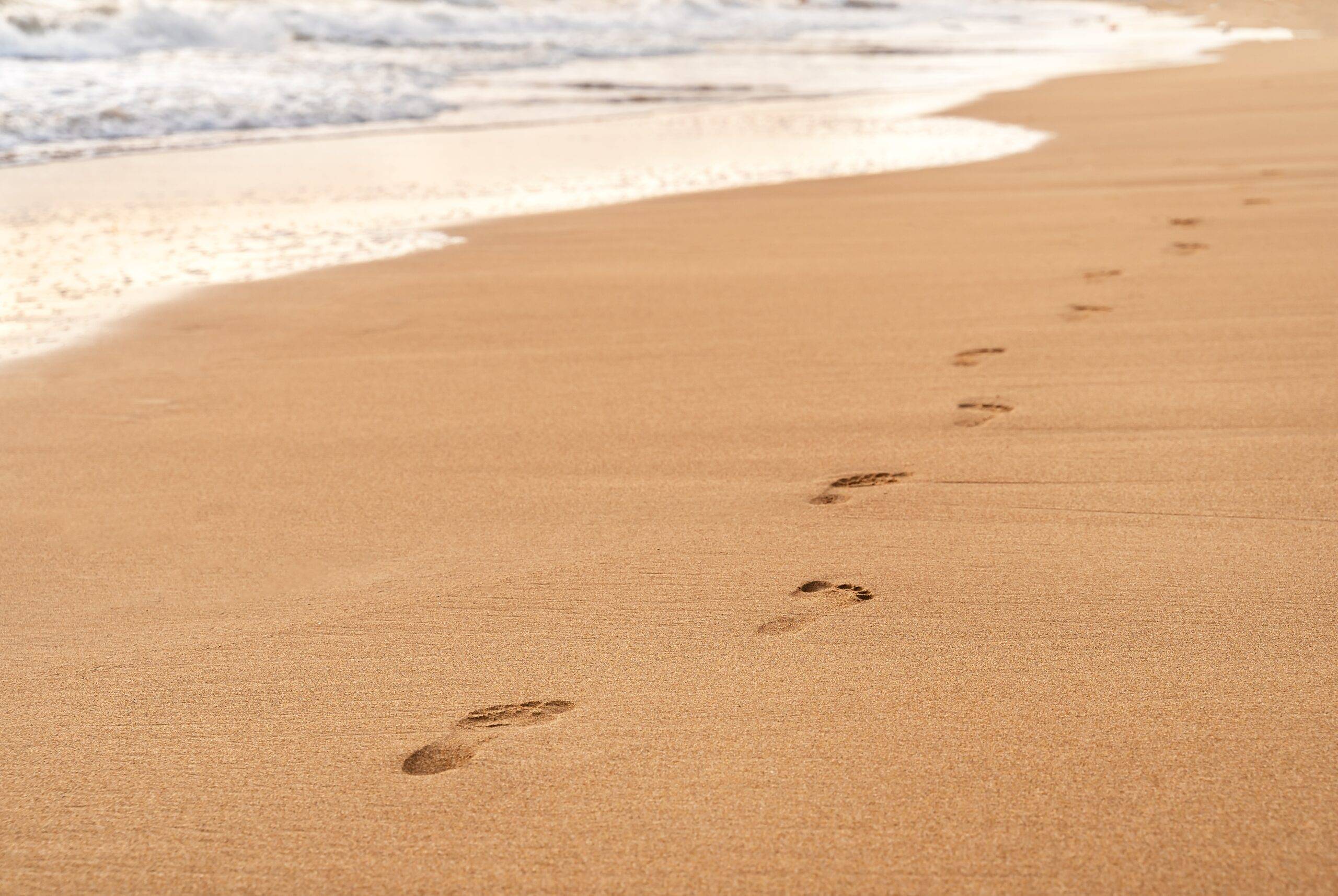 Heranrollende Wellen lassen Fußspuren im Sand verschwinden.