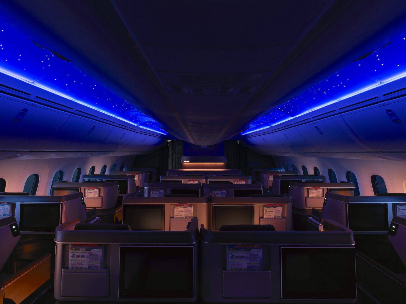 Innenansicht eines modernen Flugzeugs mit blauer Ambiente-Beleuchtung an der Decke und leeren Sitzplätzen.