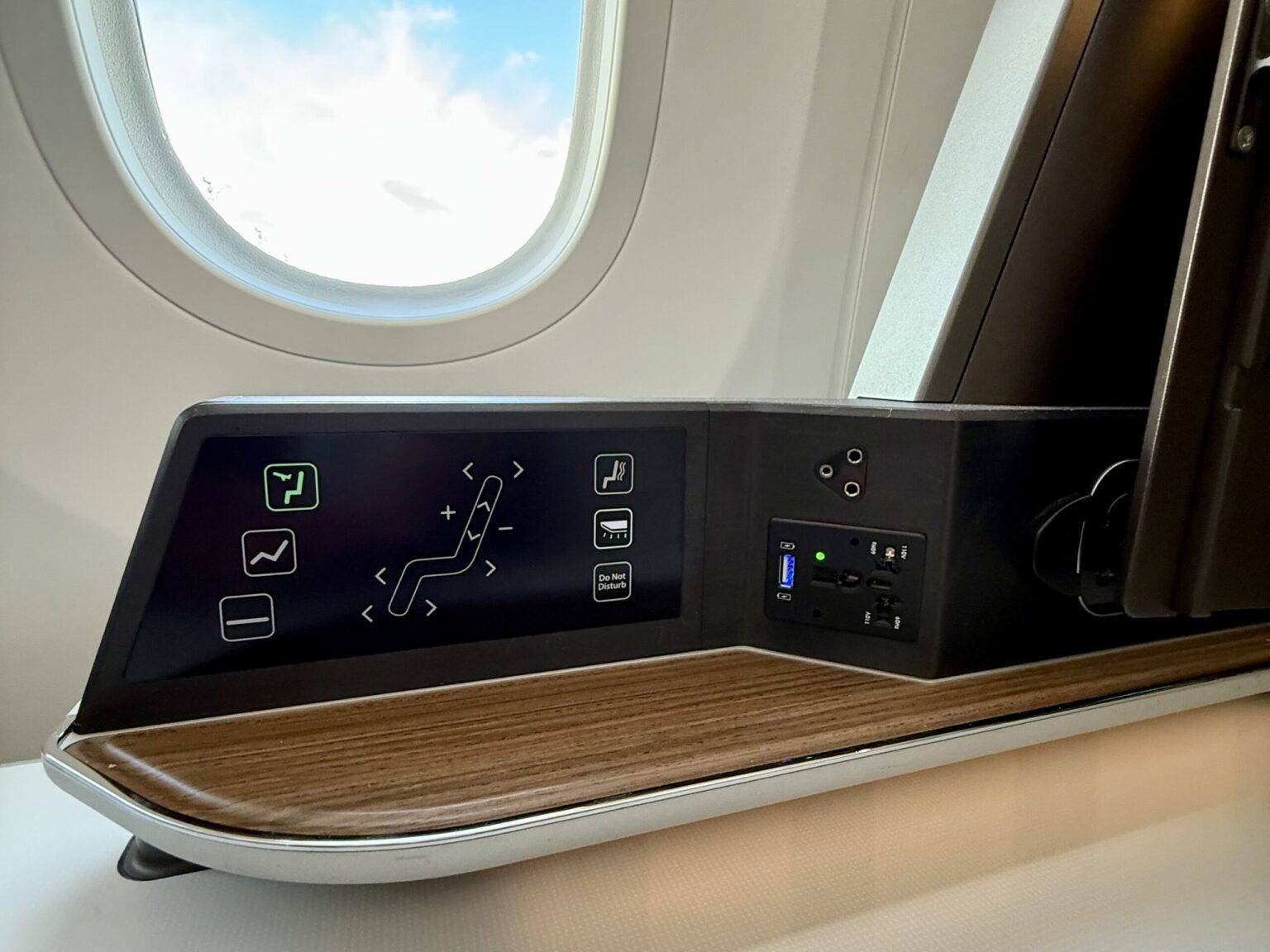 Bedienfeld mit Reglern für die Sitzeinstellung und Kabinenfunktionen, neben einem Flugzeugfenster.