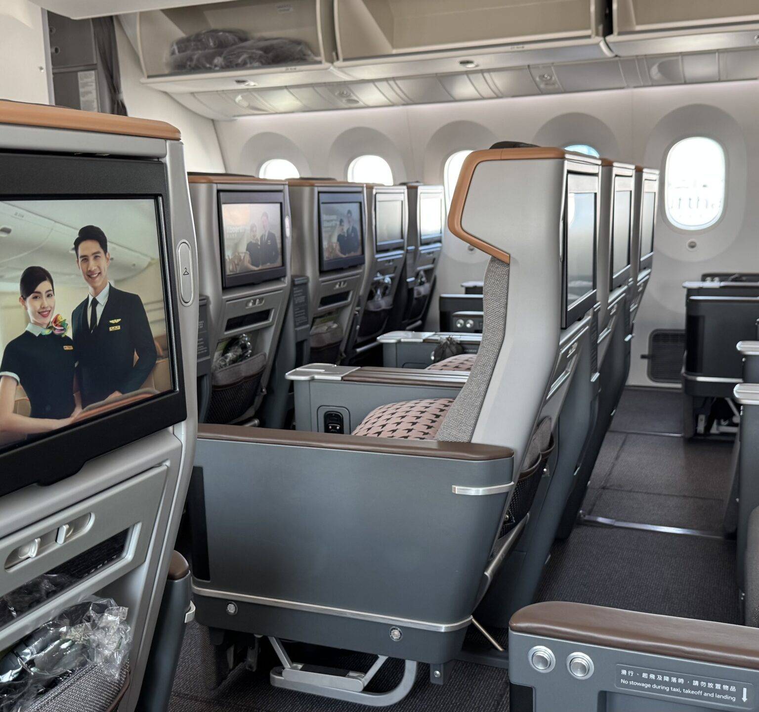 Lächelnder Passagier im Flugzeug schaut auf einen Bildschirm, auf dem eine Animation einer Wüstenlandschaft gezeigt wird. Er trägt dabei Headphones.