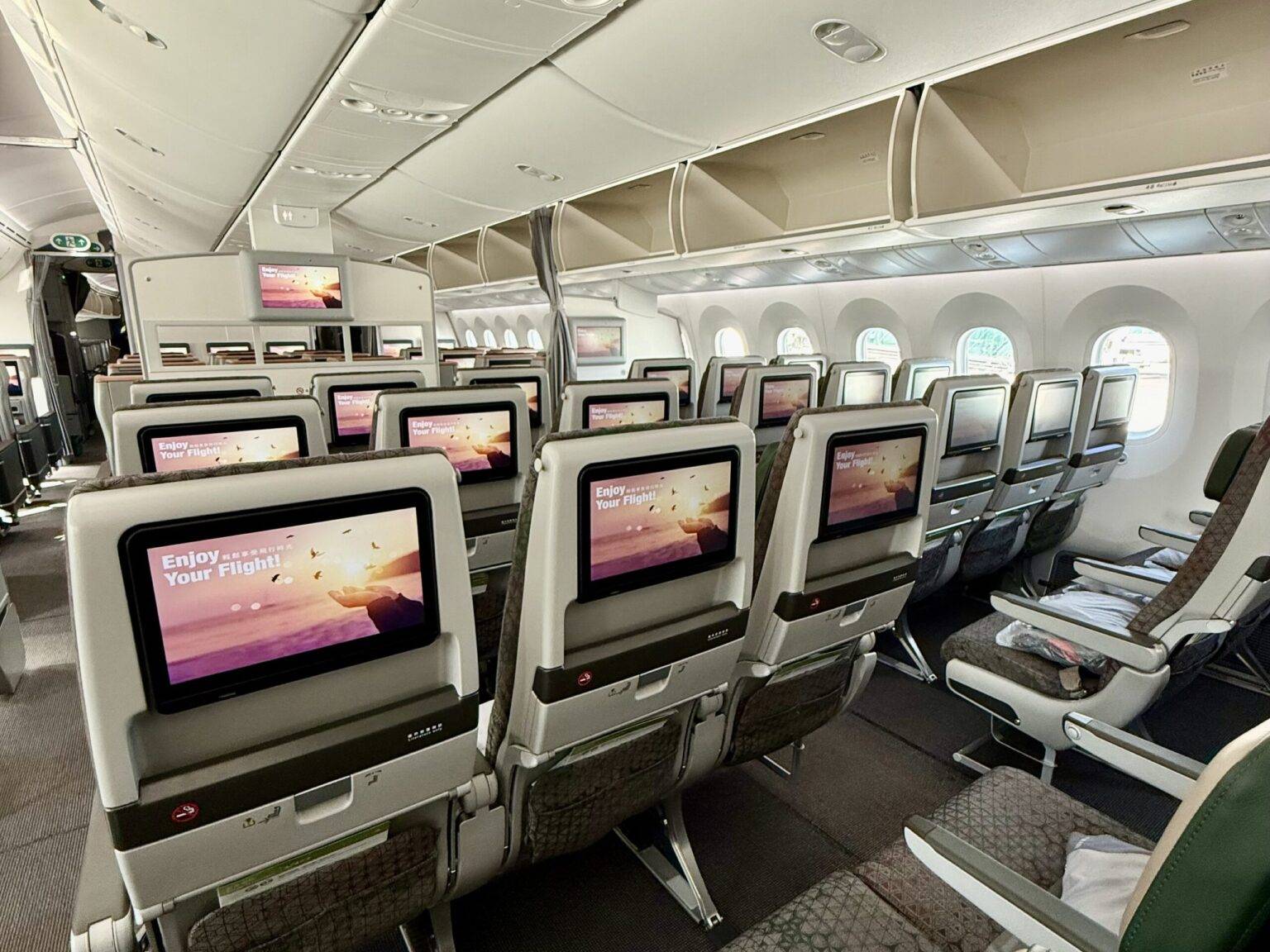 Innenansicht eines Flugzeugs mit Sitzreihen und Bildschirmen, Fenster an der Außenseite.