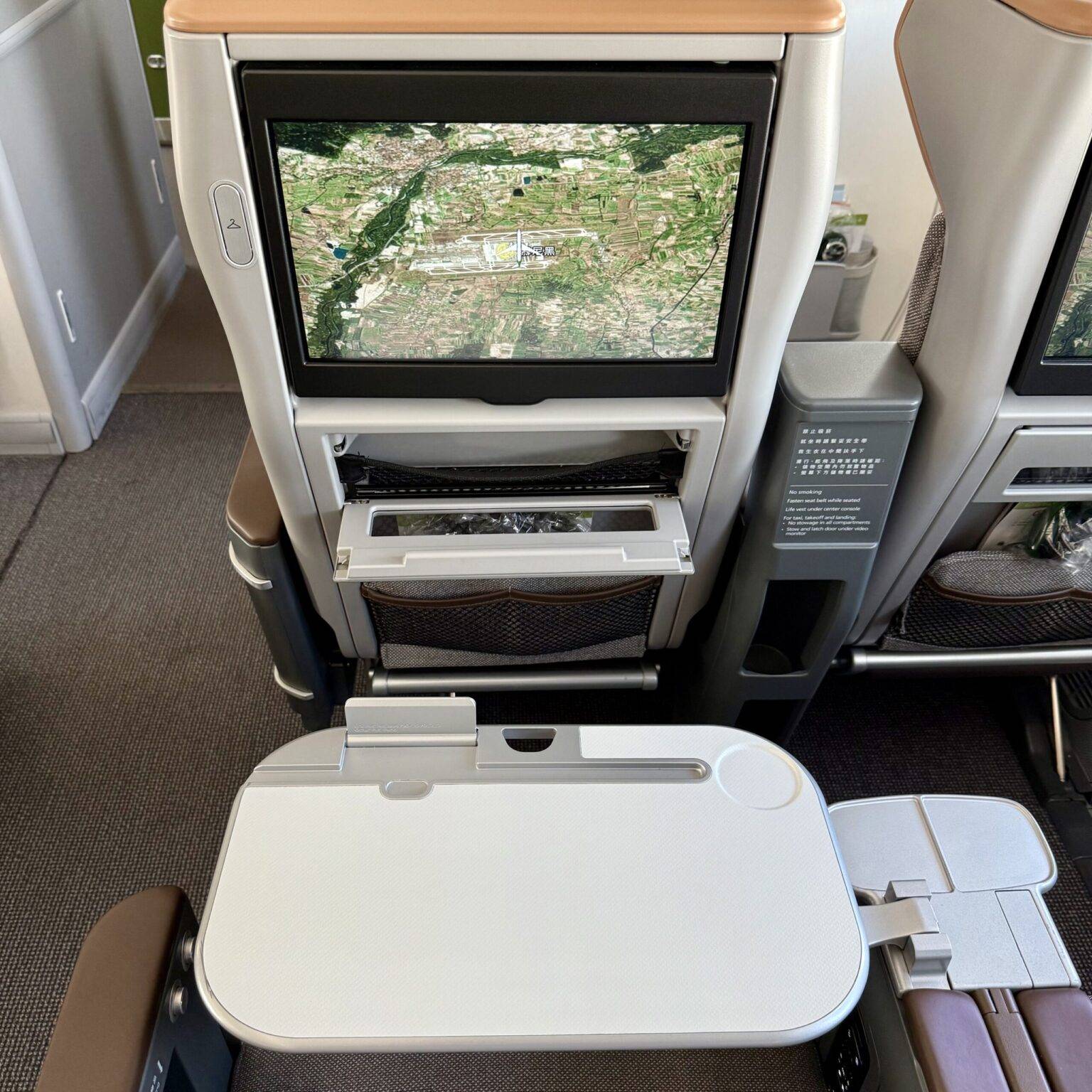 Sicht auf einen modernen Flugzeugsitz aus Passagierperspektive, mit einem Bildschirm und einem ausklappbaren Tisch.