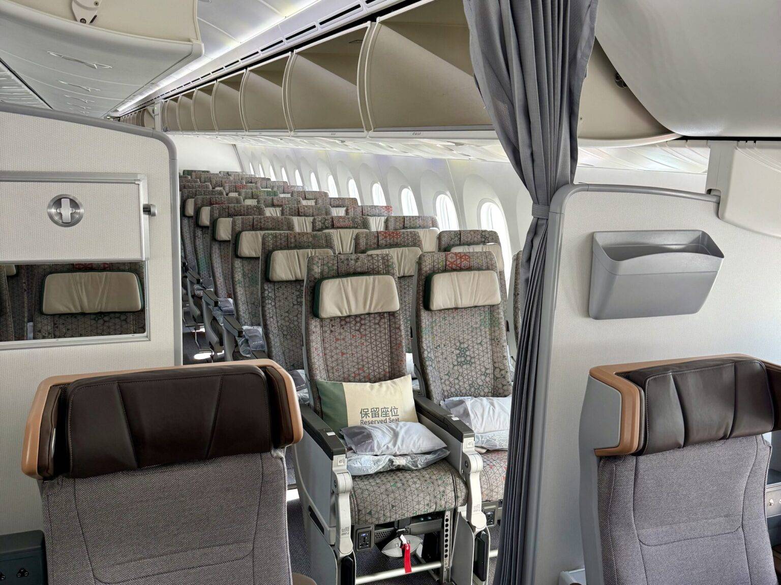 Innenansicht eines Flugzeugs mit Sitzreihen und einem Vorhang, der den vorderen Bereich abtrennt.