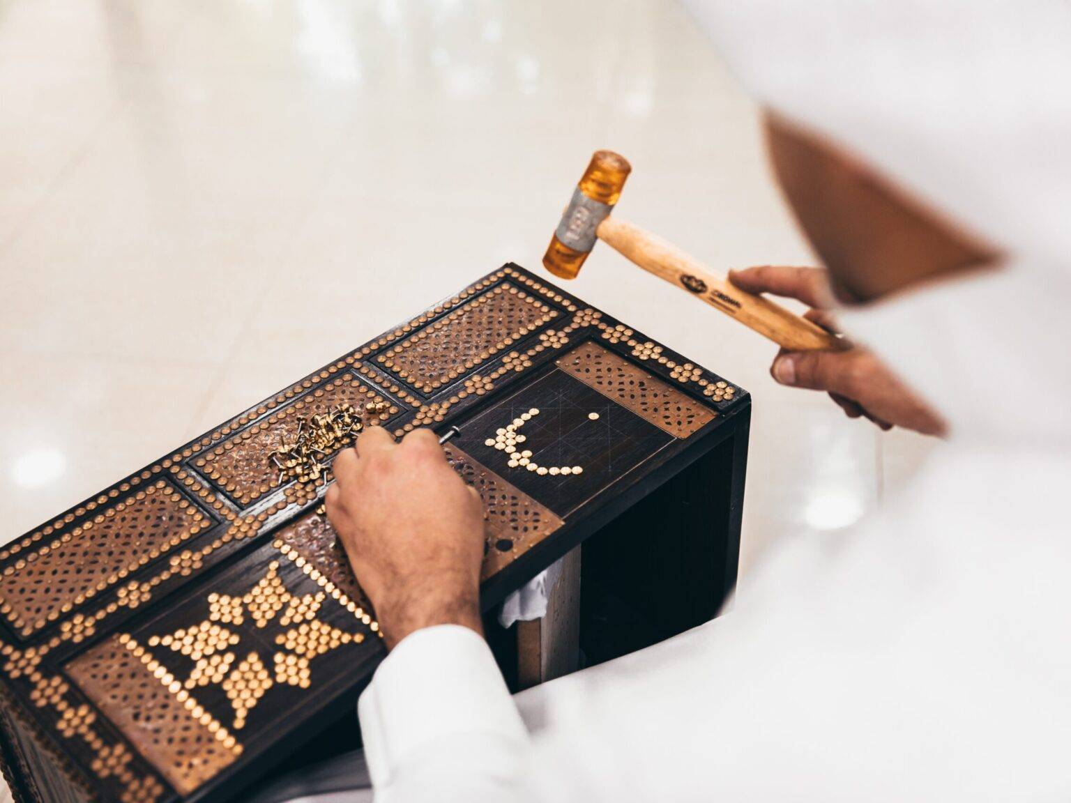 Ein Mann schlägt bronzefarbene Nägel zur Verzierung mit einem Hammer in eine schwarze Holzkiste.