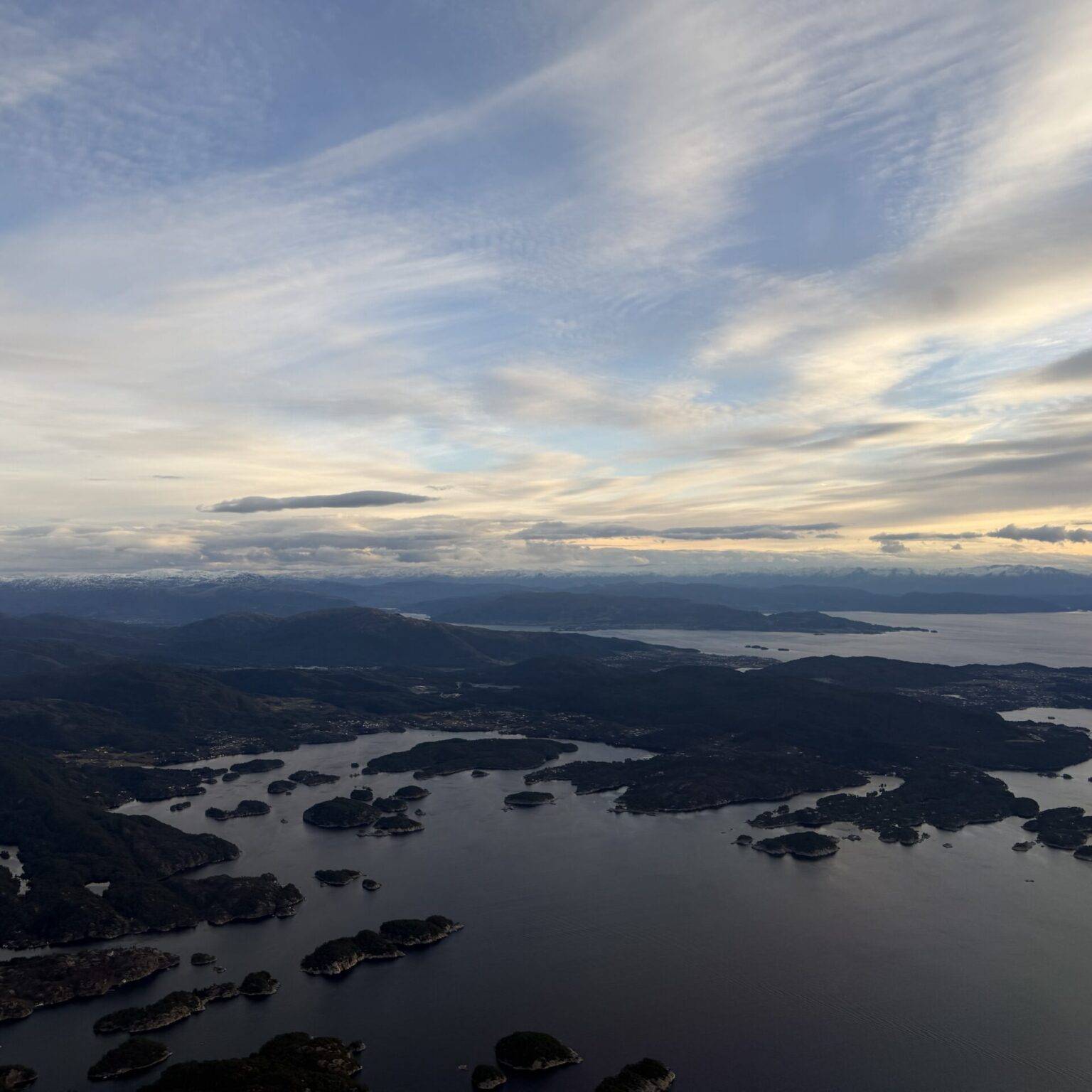 Luftaufnahme einer Küstenlandschaft mit Wasser, Inseln und einem bewölkten Himmel.