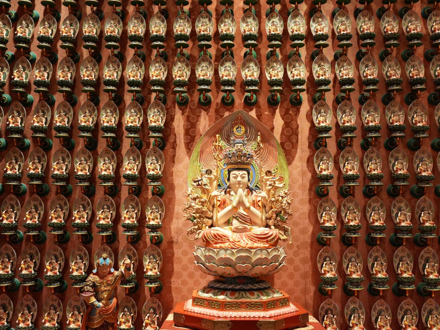 Buddhistische Statue mit vielen kleinen Figuren drumherum, an einer verzierten Tempelwand in Singapur