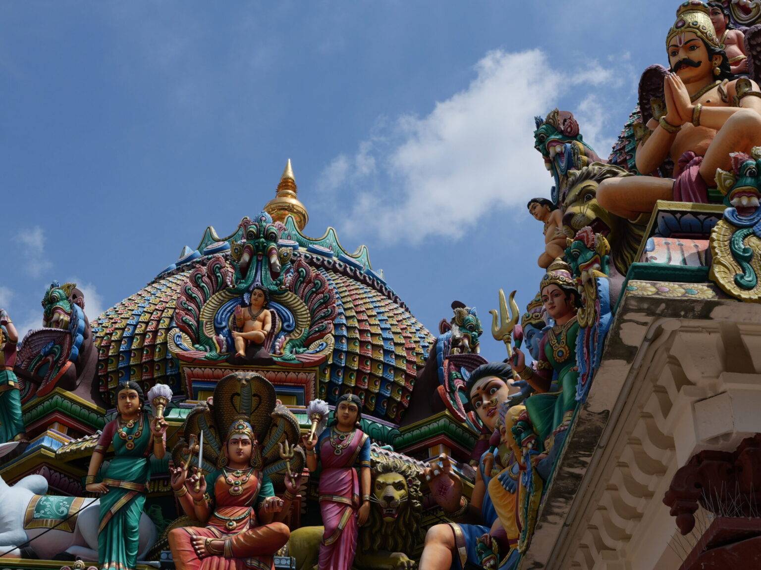 Bunte Tempelarchitektur mit Skulpturen von Göttern und mythologischen Figuren unter blauem Himmel.