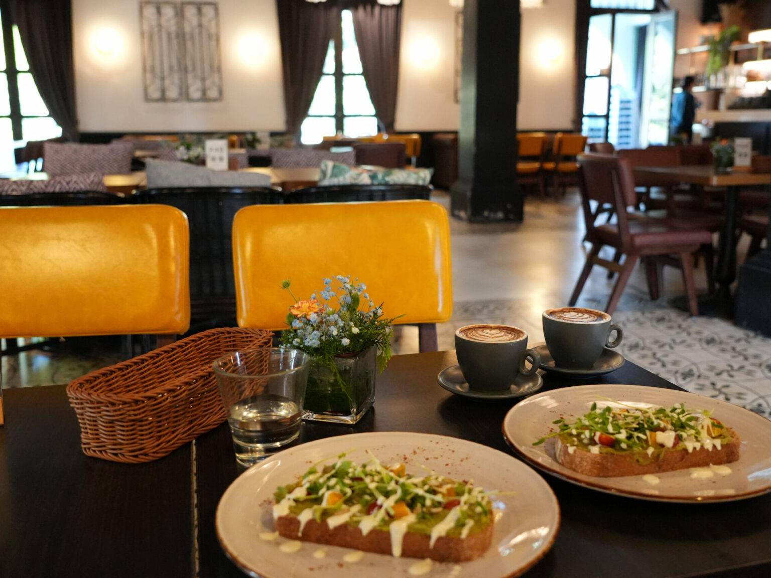 Zwei Teller mit belegtem Brot und zwei Tassen Kaffee auf einem Tisch in einem gemütlichen Café.
