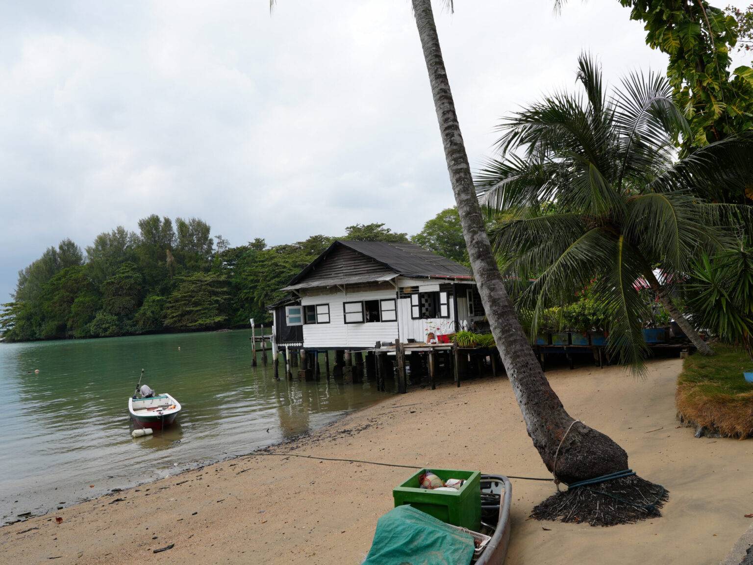 Holzhaus auf Stelzen am Wasser mit Palmenstrand auf Pulau Ubin in Singapur