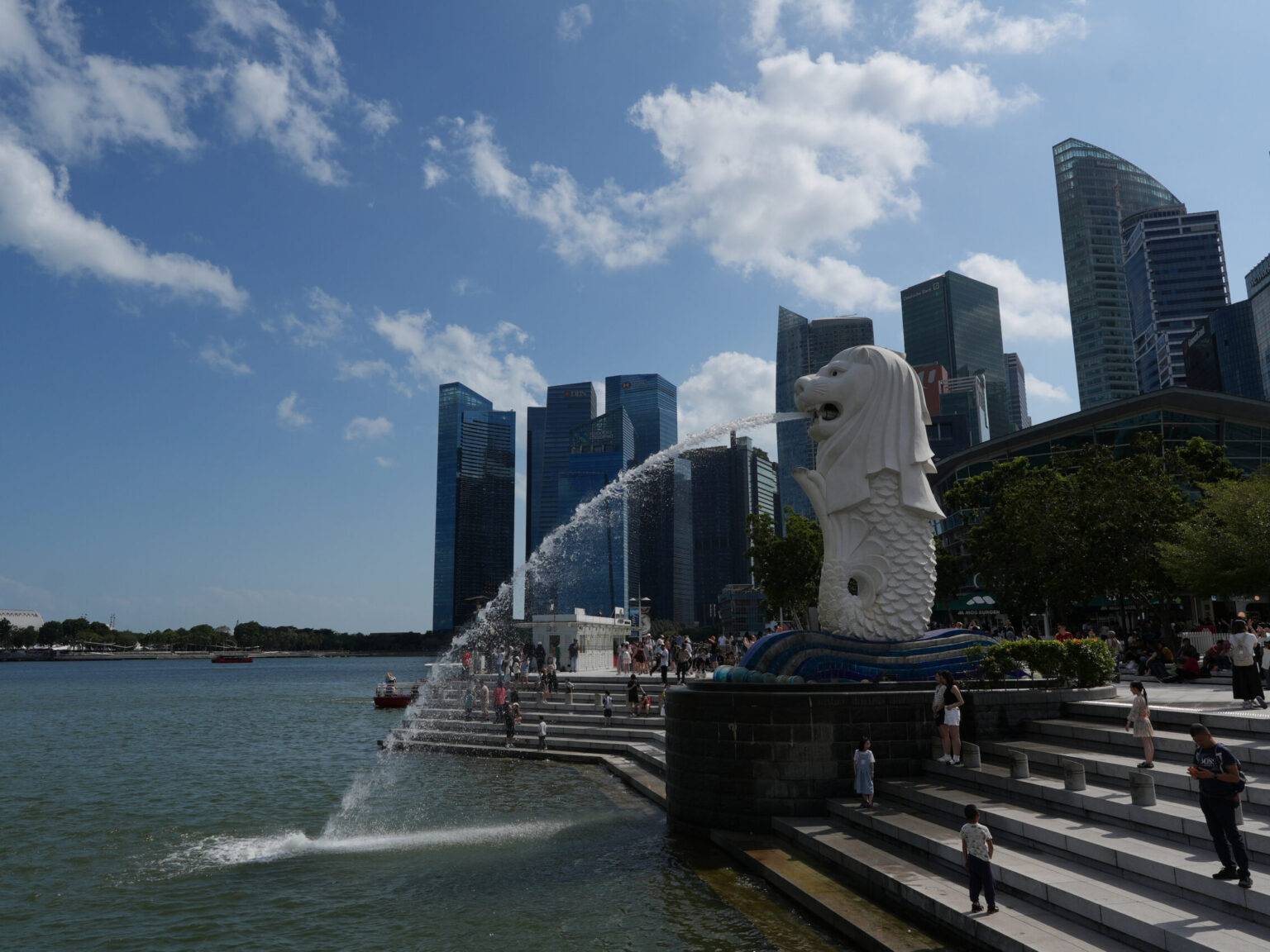 Eine Merlion-Statue, die Wasser in die Bucht spritzt, umgeben von modernen Wolkenkratzern und einem strahlend blauen Himmel.