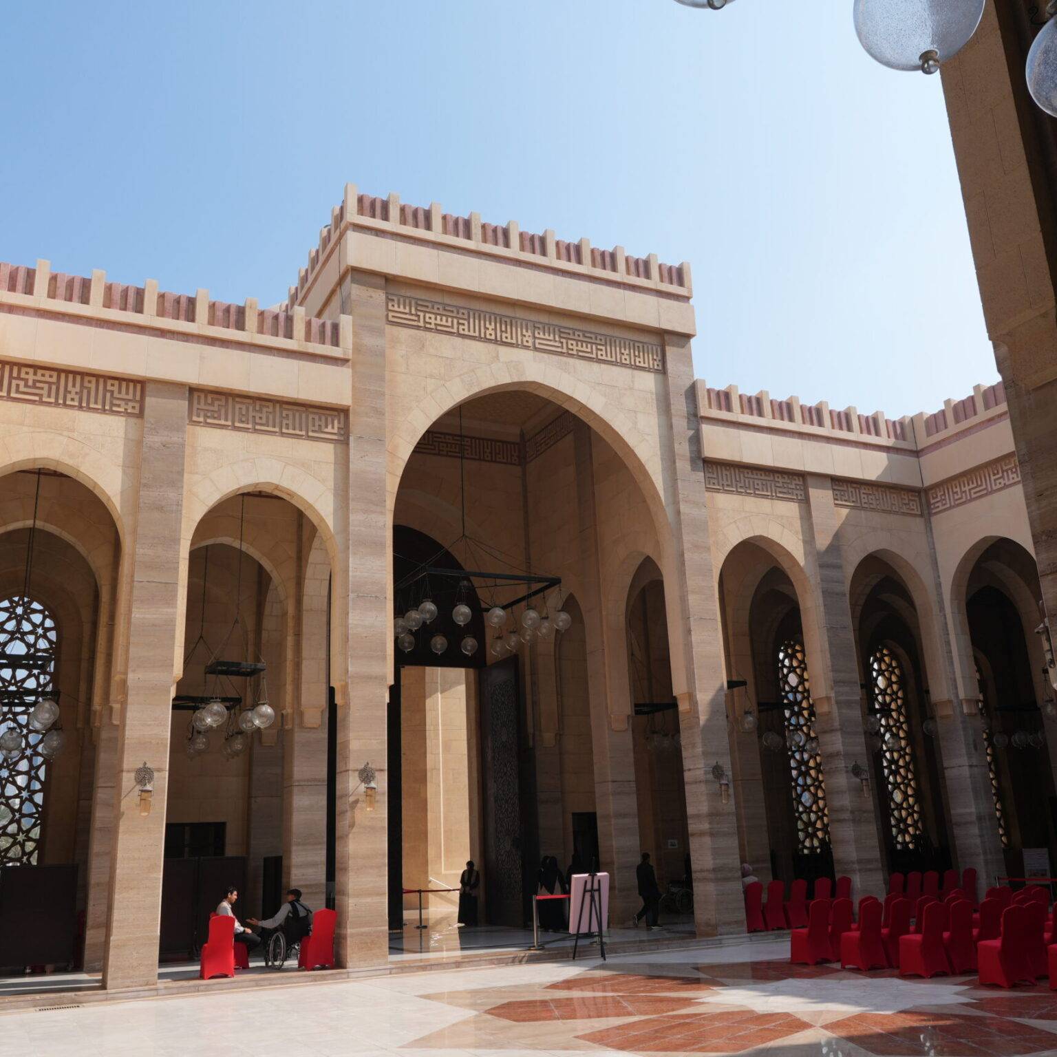 Säulengang im Innenhof der Al Fateh Grand Mosque in Manama, mit kunstvollen Bogenfenstern und Mosaikboden.