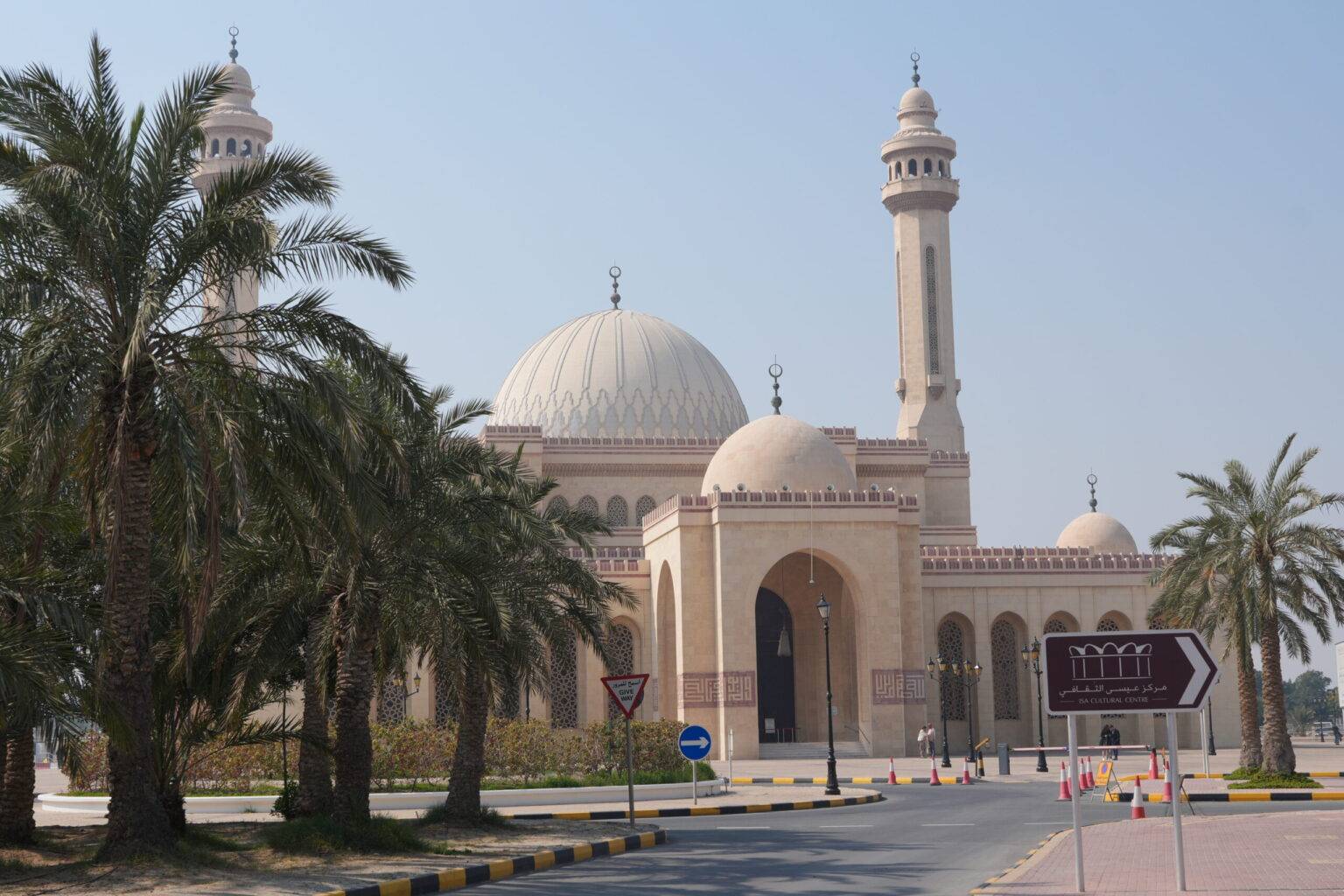 Moschee mit großen Kuppeln und Minaretten, umgeben von Palmen und einer Straße im Vordergrund.
