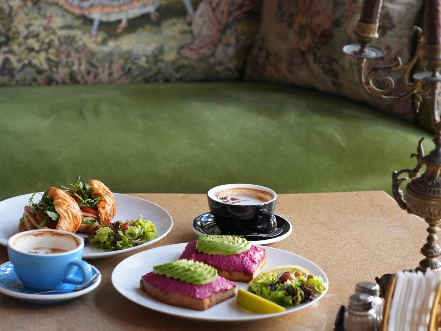 Zwei Teller mit buntem Essen und Tassen Kaffee auf einem Tisch, im Hintergrund eine grüne Bank.