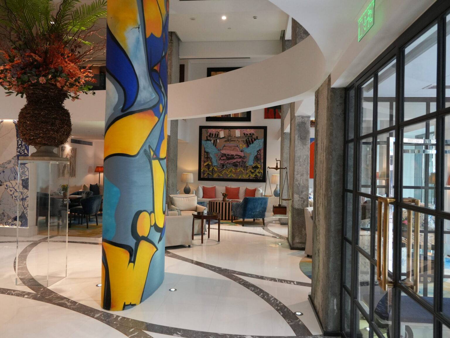 Lobby des Merchant House Manama mit farbenfroh bemalter Säule in Blau und Gelb, hellem Marmorboden und eleganter Lounge im Hintergrund