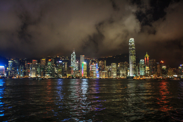 Die Lichter der Wolkenkratzer von Hongkong spiegeln sich bei Nacht im Meer.