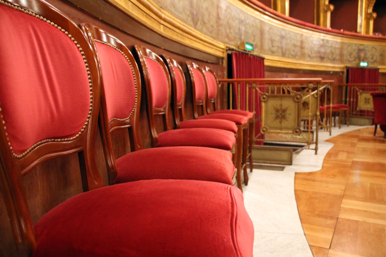 Holzstühle mit roten Samtpolstern reihen sich in Palermos Teatro Massimo an die goldene Vertäfelung der Rückwand.