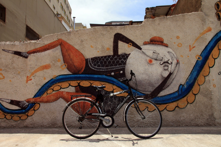 An einer gebrochenen mit Street Art verzierten Hausmauer lehnt ein Fahrrad.