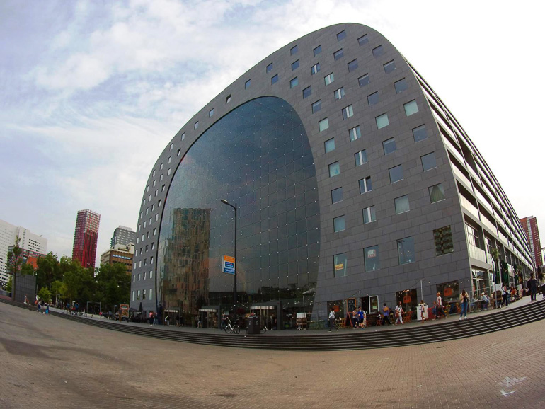 Das runde Gebäude des Rotterdamer Markthal besticht durch seine runde Glasfassade und den vielen viereckigen kleineren Fenstern darüber.