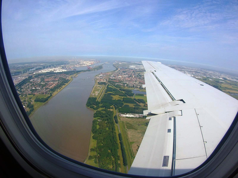 Der Blick aus dem Flugzeugfenster zeigt einen Fluss, der ins Meer mündet und den Hafen Rotterdams.