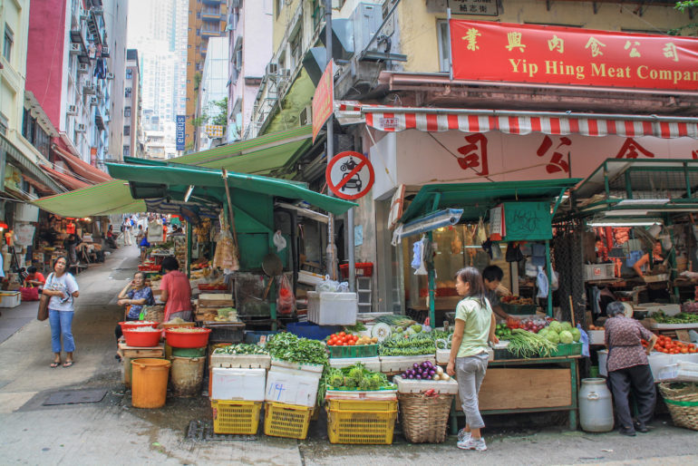An einem Straßeneck in Hongkong sind Stände mit Obst und Gemüse zum Verkauf aufgebaut.