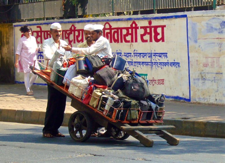 Auf einer Straße vor dem Bahnhof Churchgate in Mumbai richten Dabawallas verpackte Essenboxen auf einen Holzkarren.