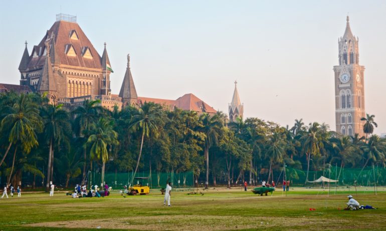 Auf den Grünflächen von Mumbais Oval Maidan in Fort wird vor der Kulisse alter Kolonialgebäuden Cricket gespielt.