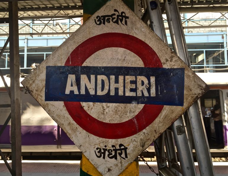 Ein Schild mit blau-weißer Aufschrift und rotem Rand am Bahnhof von Mumbai zeigt den Andheri Zug an.